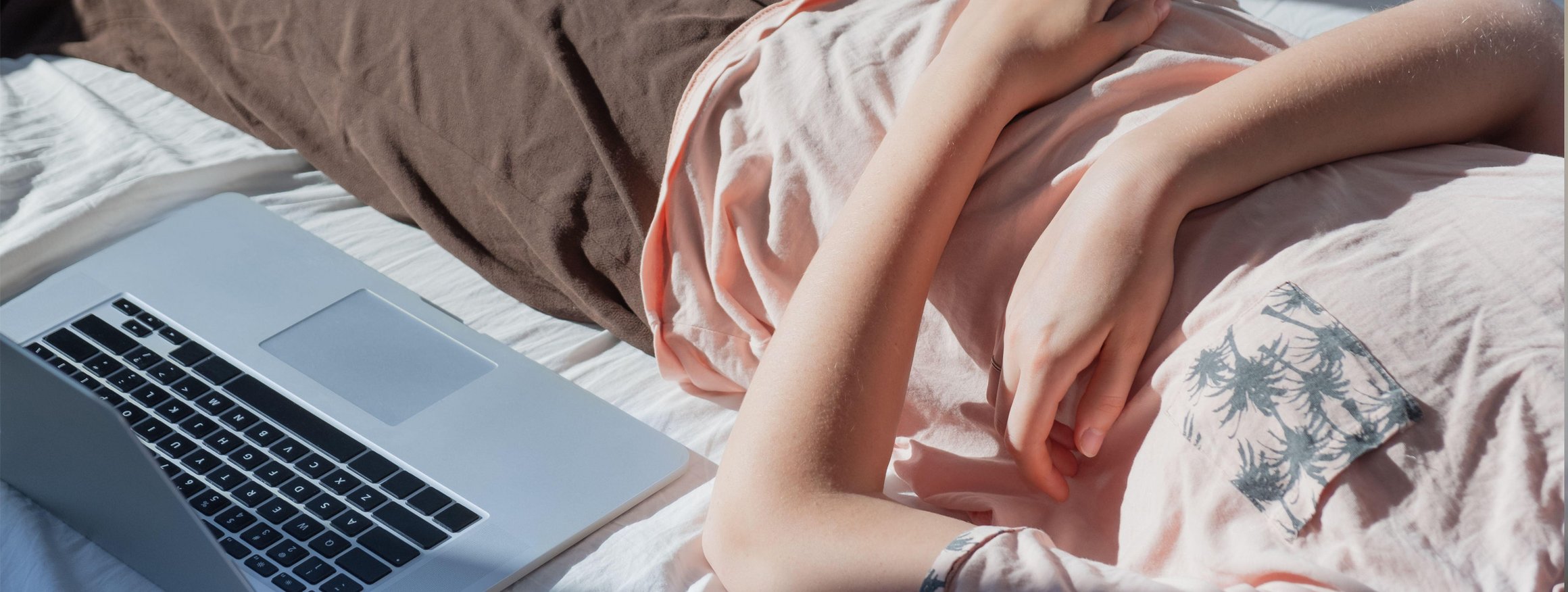 Das Foto zeigt den Ausschnitt einer Person, die neben ihrem Laptop auf dem Bett liegt.