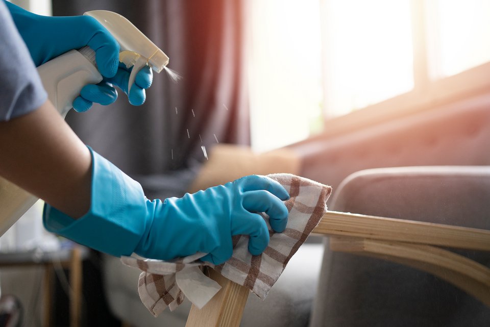 Eine weibliche Reinigungskraft mit blauen Gummihandschuhen reinigt eine Stuhllehne