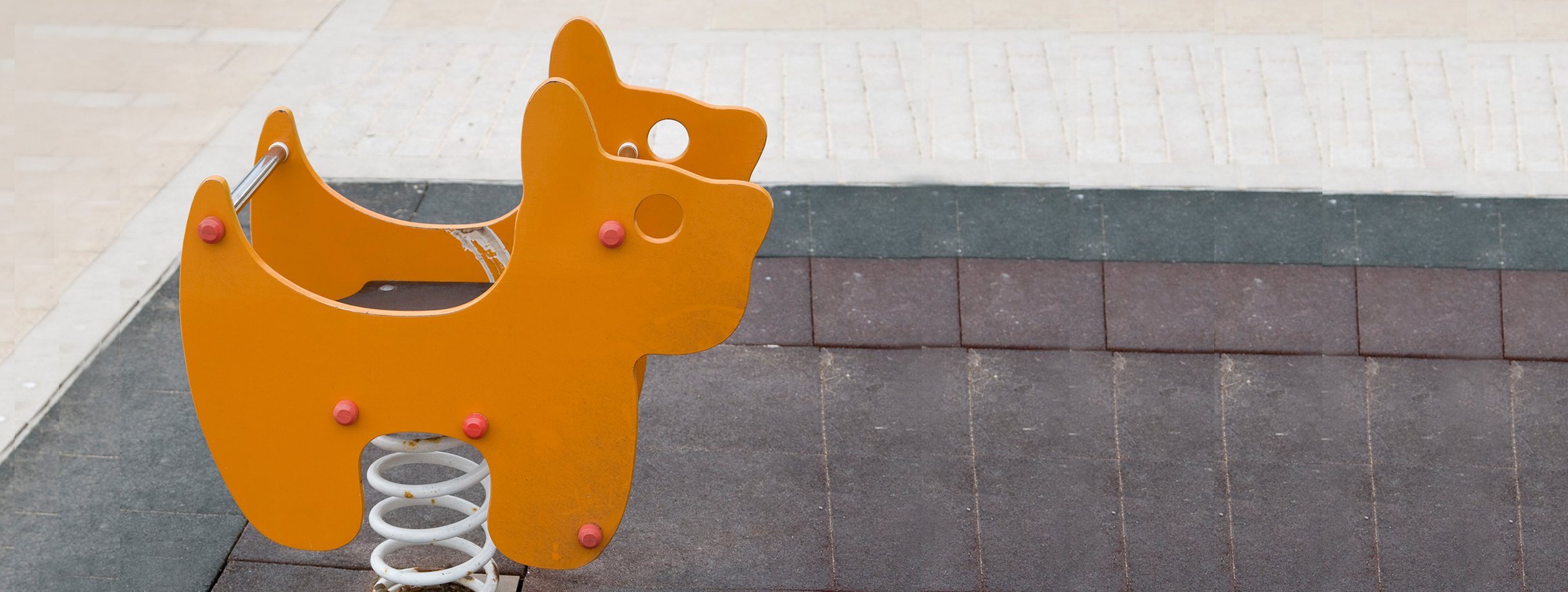 Ein orangefarbenes Wippgerät in Tierform steht auf einem Kinderspielplatz und der Boden ist betoniert
