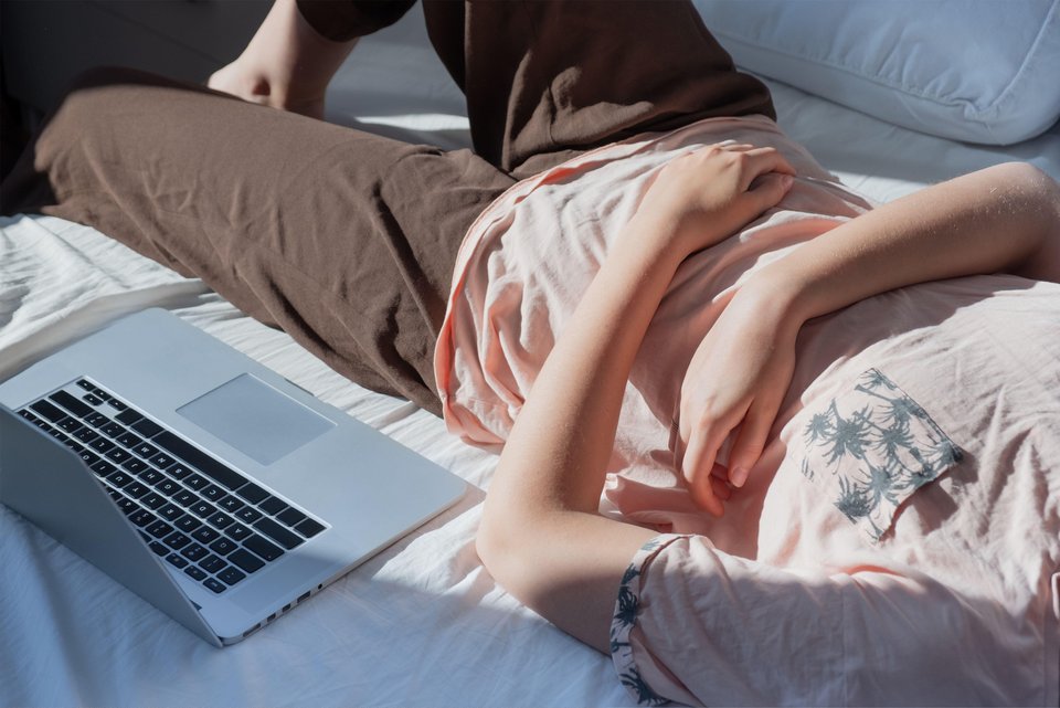 Das Foto zeigt den Ausschnitt einer Person, die neben ihrem Laptop auf dem Bett liegt.