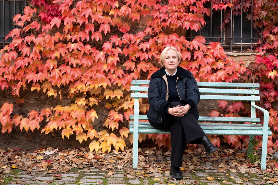 Die Schriftstellerin Anne Rabe sitzt auf einer Bank vor einer Hauswand mit herbstlichem Efeu