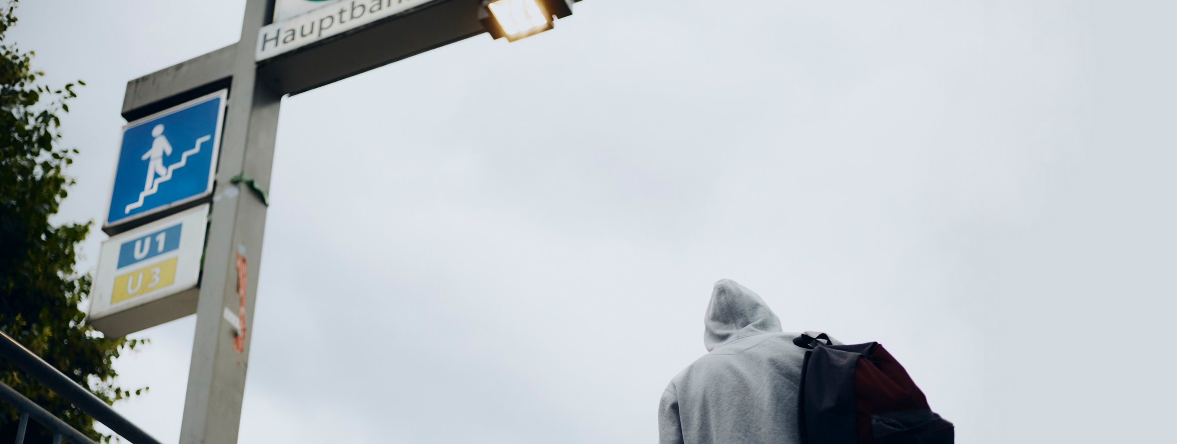 Ein Mann steht im Kapzen-Hoodie und Rucksack vor der Treppe einer U-Bahn-Station