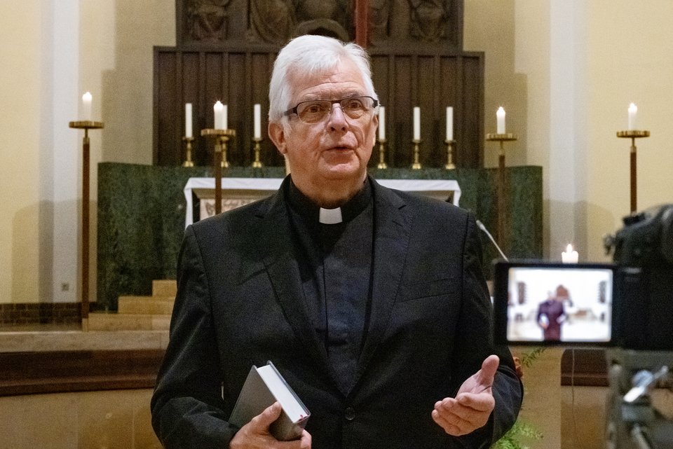 Ein Pfarrer steht vor dem Altar in einer Kirche und spricht und wird dabei gefilmt