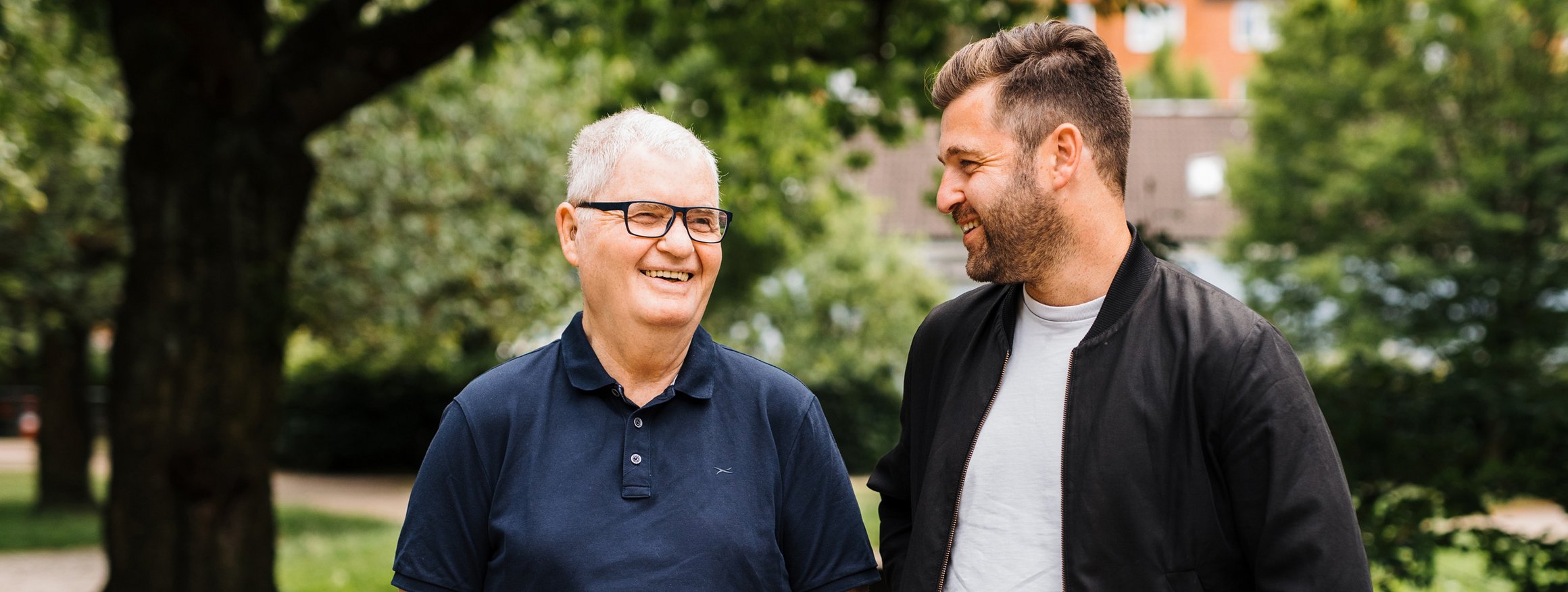 Das Foto zeigt Vater und Sohn, die an einer Tischtennisplatte gelehnt miteinander lachen.