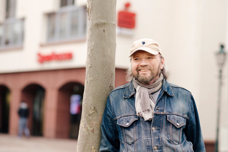 Der ehemalige Bistrobetreiber, Norbert Kestel, steht an einem Baum gelehnt vor einer Sparkasse