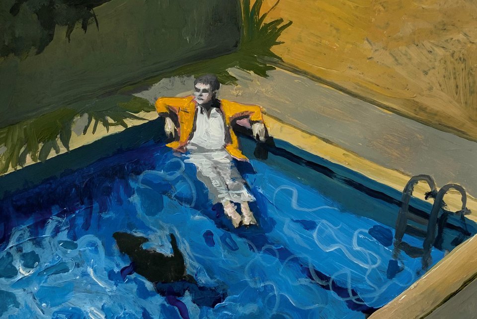 Das Bild zeigt einen Mann, der angezogen im Pool sitzt, neben ihm ein Hund schwimmend