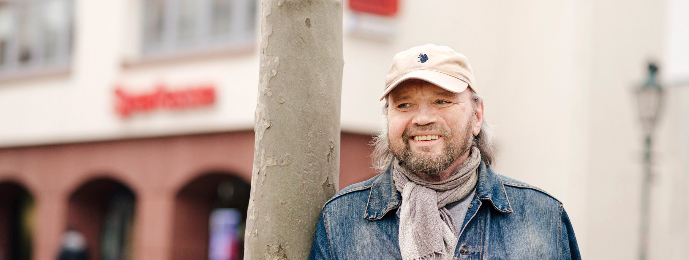 Der ehemalige Bistrobetreiber, Norbert Krestel, steht an einem Baum gelehnt vor einer Sparkasse