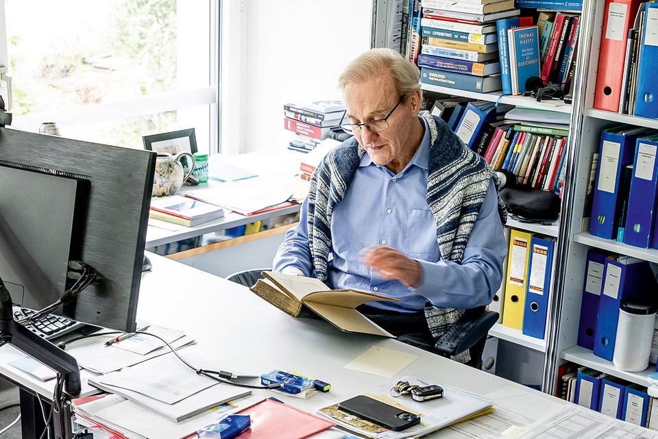 Der Wirtschaftswissenschaftler und Professor, Ernst Fehr, sitzt an seinem Arbeitsplatz am Institut für Volkswirtschaftslehre an der Uni Zürich und  hält ein Buch in den Händen 