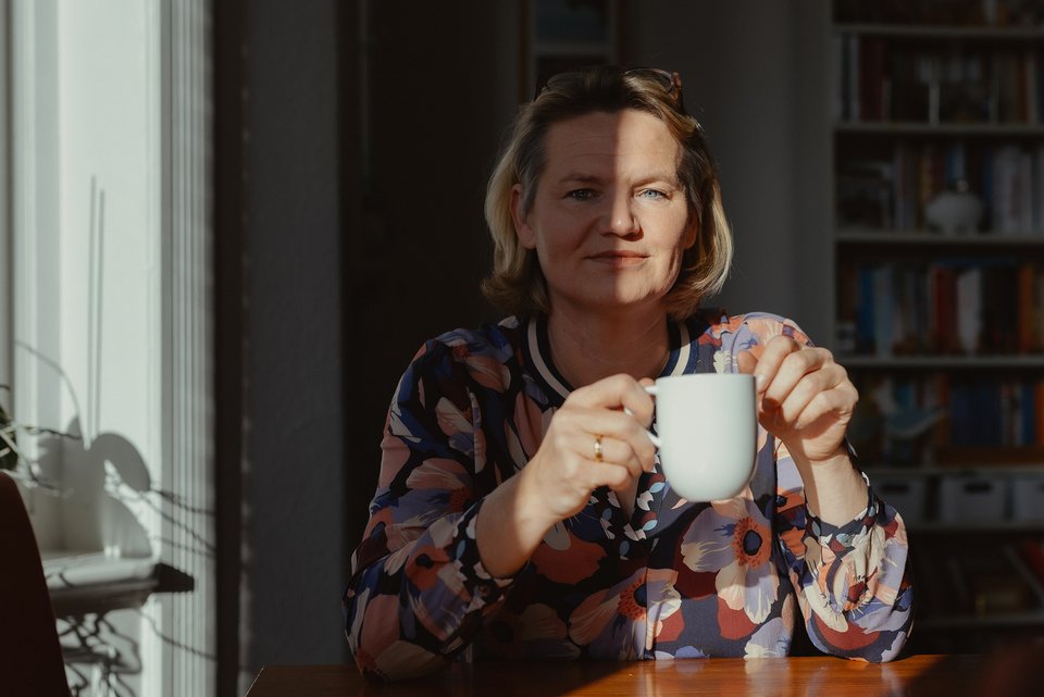 Sandra Schumacher sitzt im Halbschatten an einem Tisch und hält eine weiße Tasse in der Hand und ist froh, dass sie seit 20 Jahren ohne Alkohol lebt