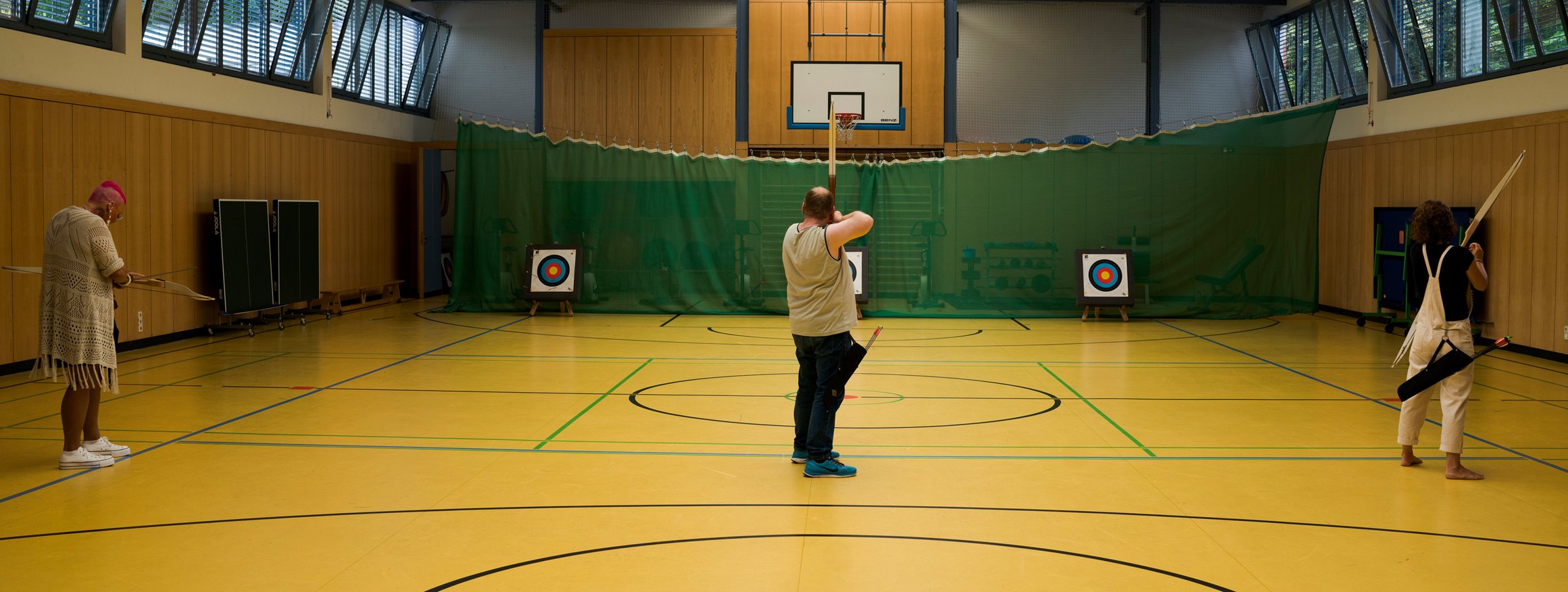 Patientinnen und Patienten in einer Sporthalle beim therapeutischen Bogenschießen