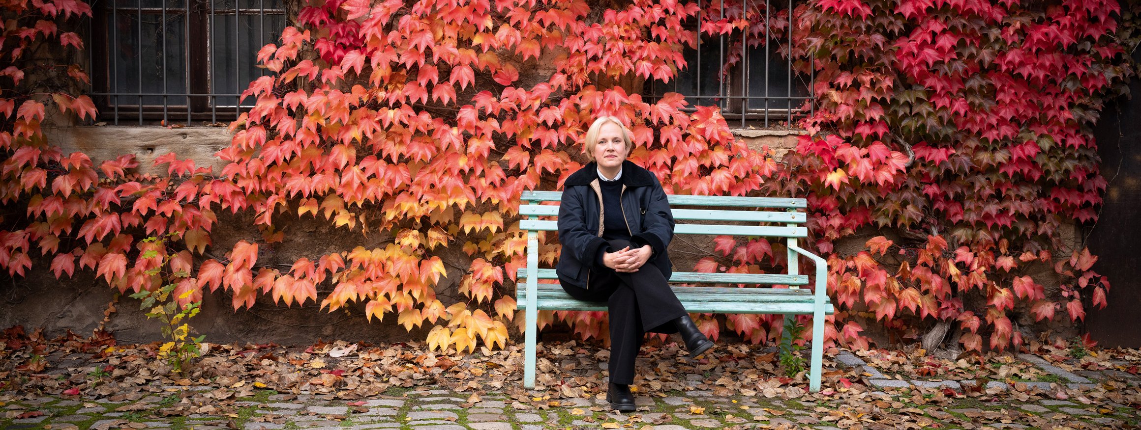 Die Schriftstellerin Anne Rabe sitzt auf einer Bank vor einer Hauswand mit herbstlichem Efeu