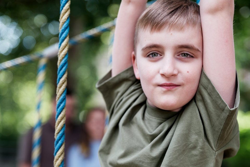 Ein Junge mit Autismus-Spektrum-Störung ist auf einem Spielplatz und hält sich an einem Spielgerüst fest