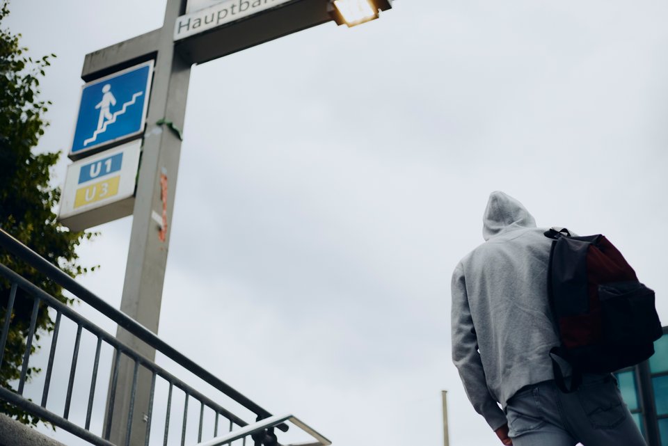 Ein Mann steht im Kapzen-Hoodie und Rucksack vor der Treppe einer U-Bahn-Station