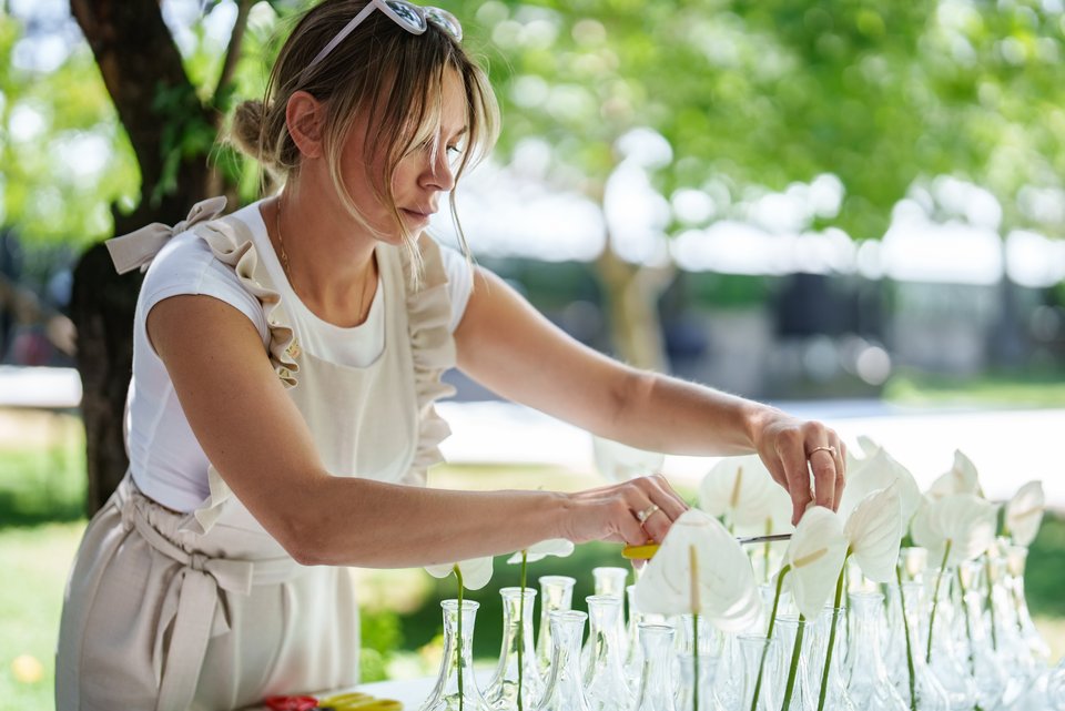 Eine Hochzeitsplanerin richtet in einem Garten bei schönem Wetter nachdenklich einen Hochzeitstisch her