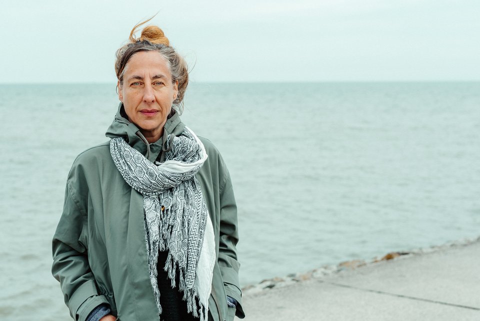 Die Schriftstellerin Judith Herrmann steht mit Mantel und Schal an einem Strand, hinter ihr das graue Meer