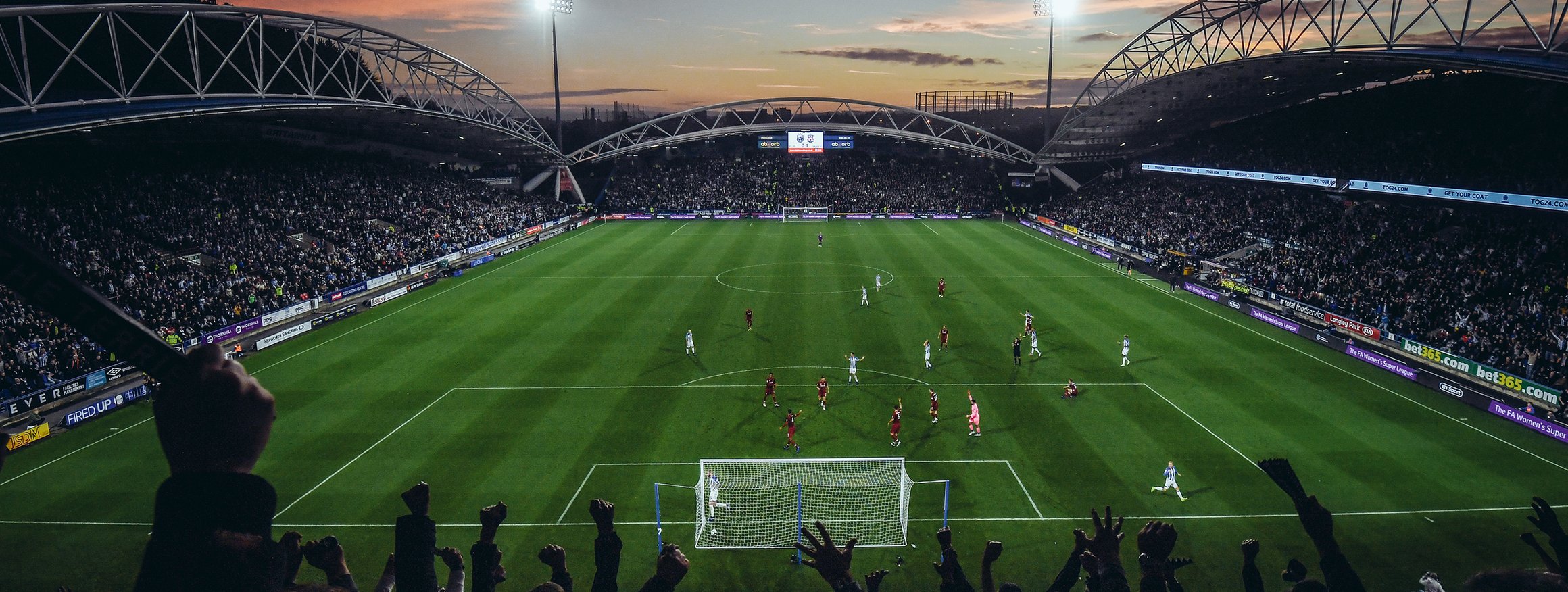 Ein Fußball-Stadion mit vielen Menschen auf der Tribüne in der Abenddämmerung