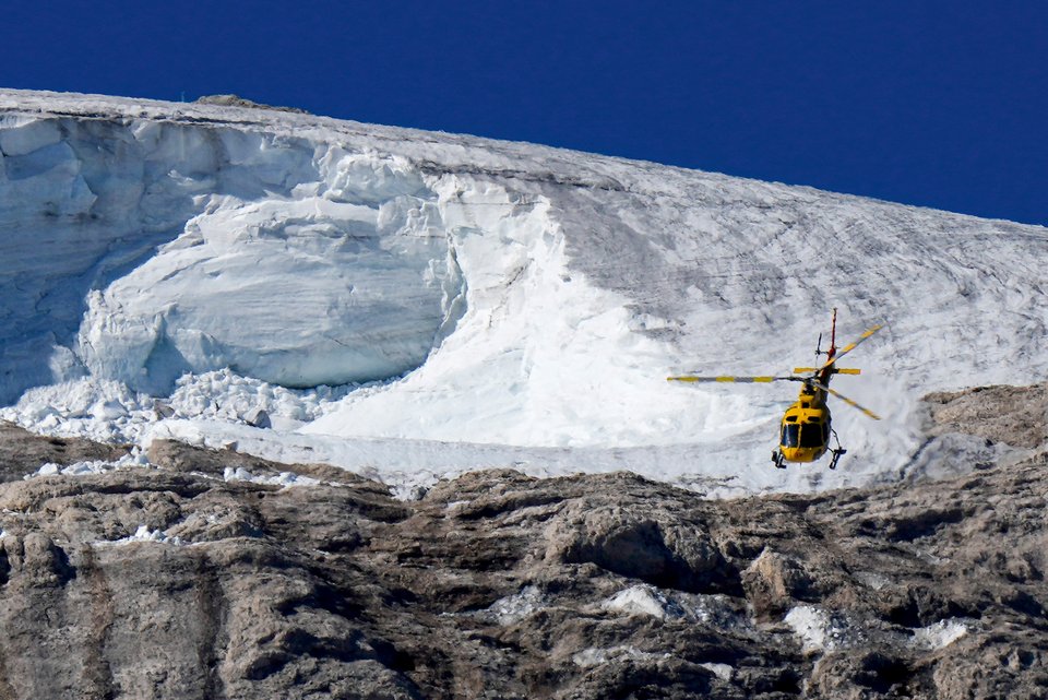 Ein Rettungshubschrauber im Einsatz in den Dolomiten, dahinter ein Gletscher