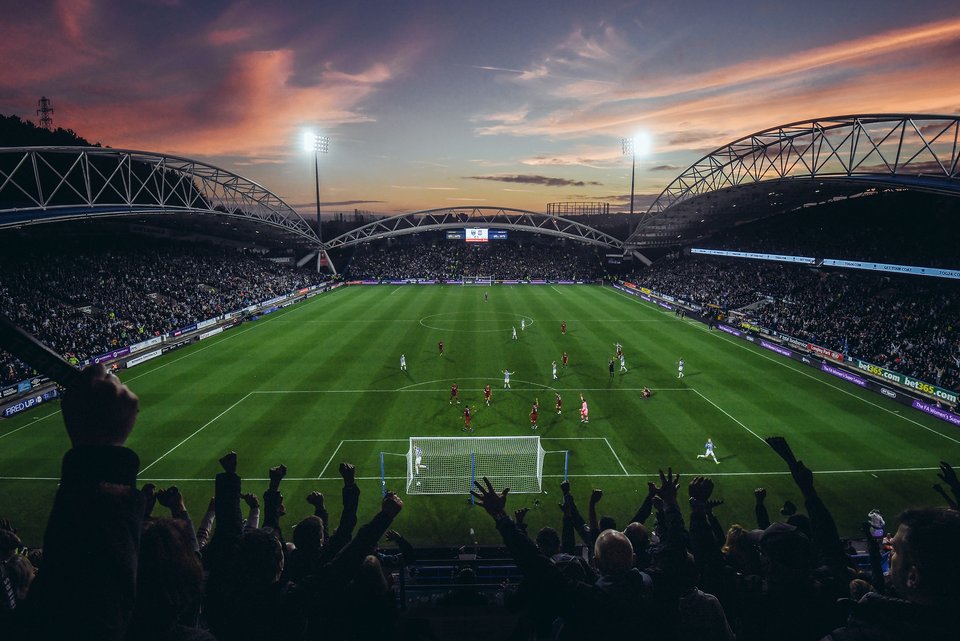 Ein Fußball-Stadion mit vielen Menschen auf der Tribüne in der Abenddämmerung