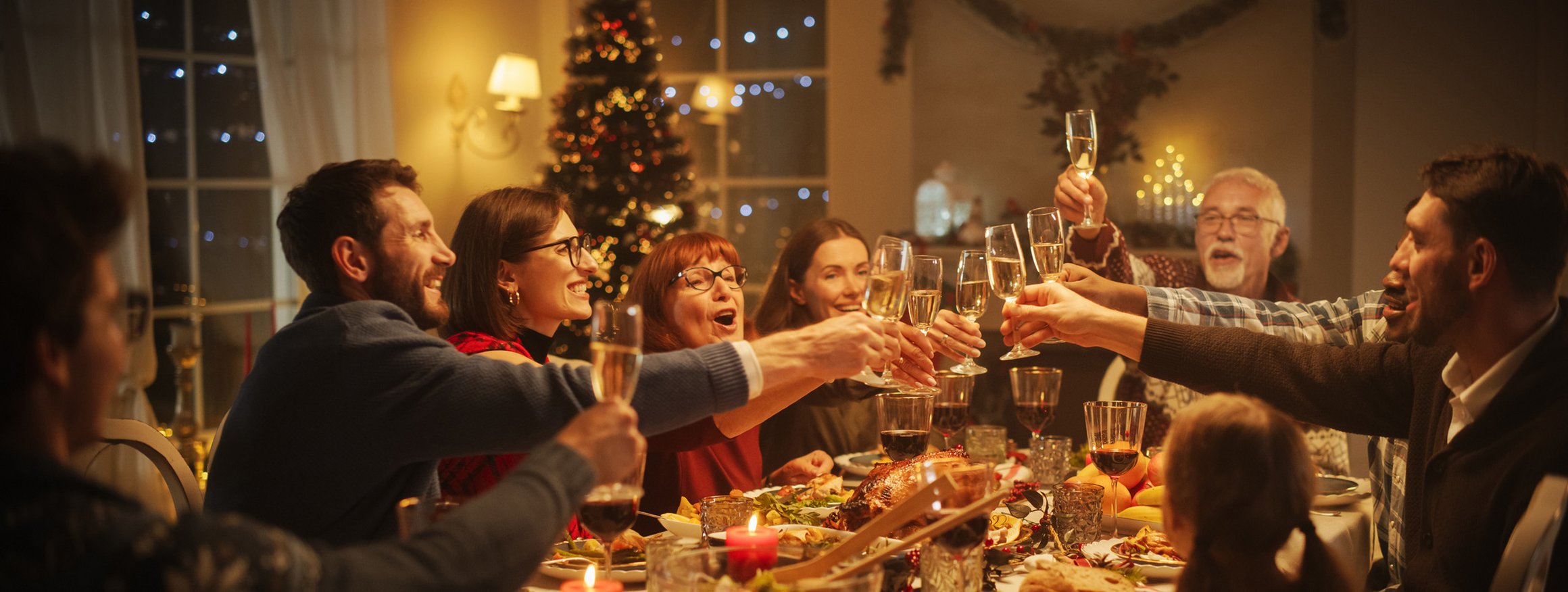 Eine Familie sitzt an Weihnachten am festlich gedeckten Tisch und prostet sich zu.