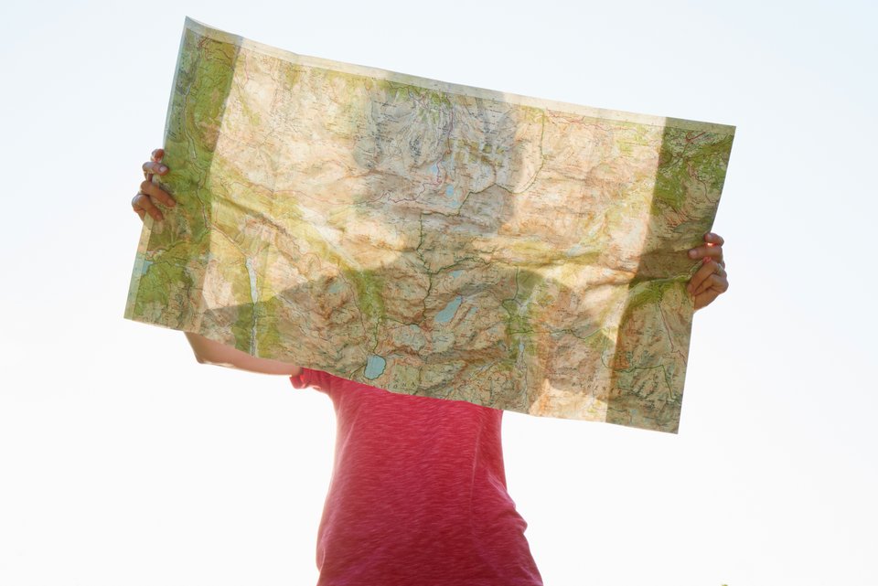 Eine Frau hält eine Landkarte in den Händen vor ihr Gesicht