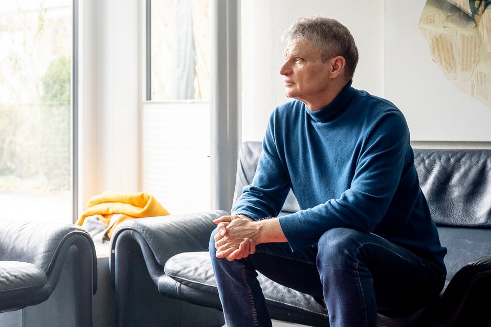 Der Psychologie Guy Bodenmann sitzt auf einen Sofa udn schaut dabei aus dem Fenster