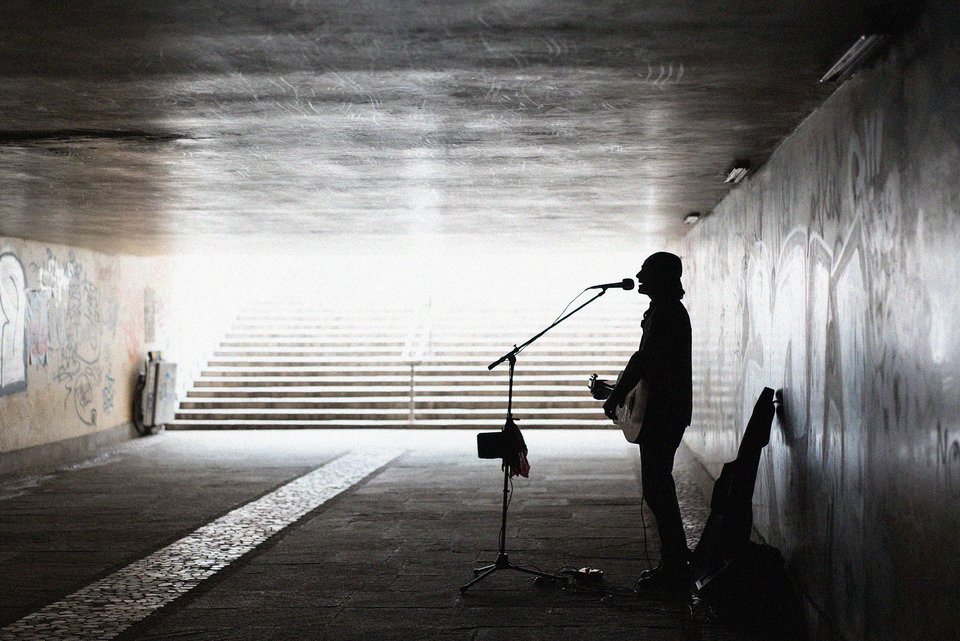 Ein Straßenmusiker steht allein in einer Unterführung mit seiner Gitarre und singt in ein Mikrofon