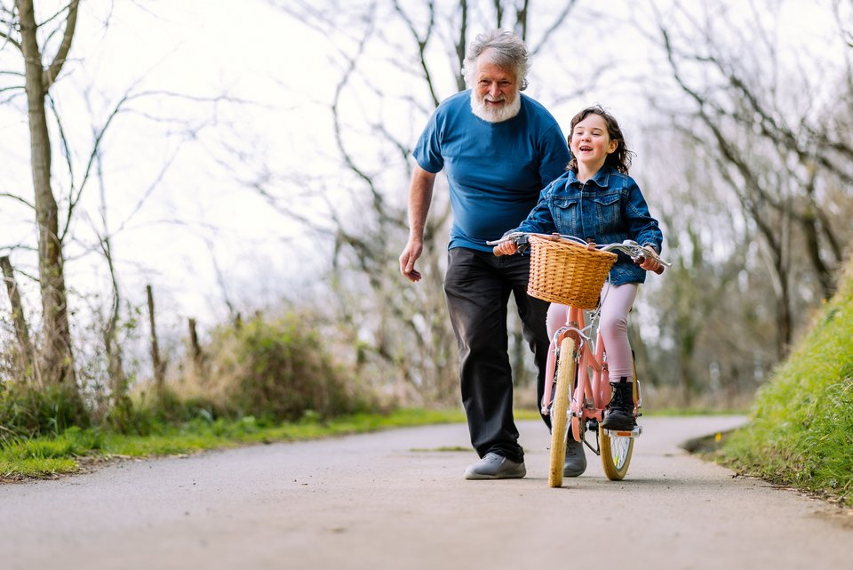 Ein Großvater bringt seiner Enkeltochter das Radfahren bei und beide lachen dabei