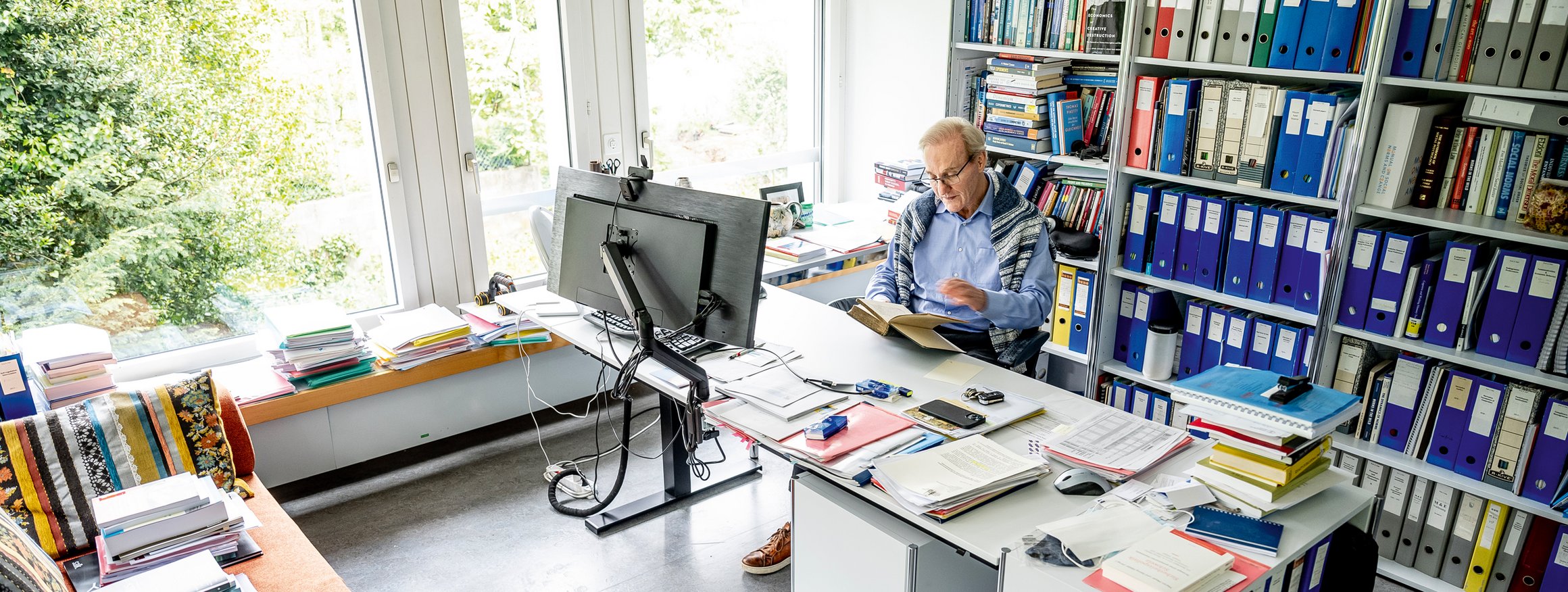 Der Wirtschaftswissenschaftler und Professor, Ernst Fehr, sitzt an seinem Arbeitsplatz am Institut für Volkswirtschaftslehre an der Uni Zürich und  hält ein Buch in den Händen 