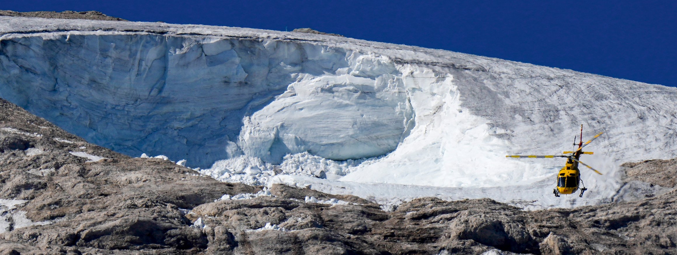 Ein Rettungshubschrauber im Einsatz in den Dolomiten, dahinter ein Gletscher