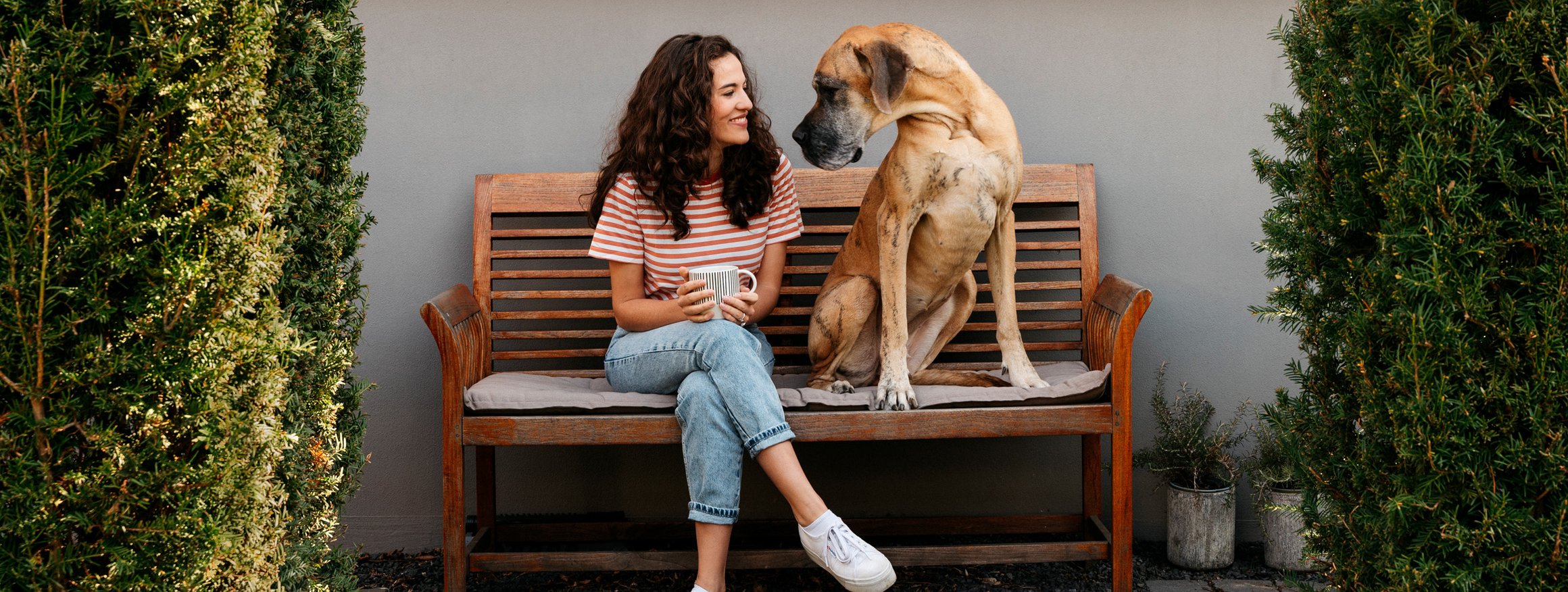 Die Journalistin und Moderatorin Mona Ameziane sitzt gemeinsam mit einer großen Dogge der Nachbarin auf einer Bank und lächelt sie an, da durch sie die Angst vor Hunden weniger geworden ist