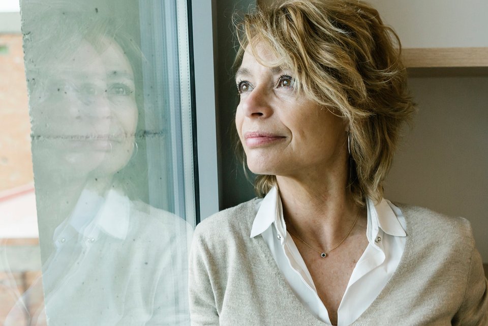 Foto zeigt eine ältere Frau, die nachdenklich aus dem Fenster schaut 