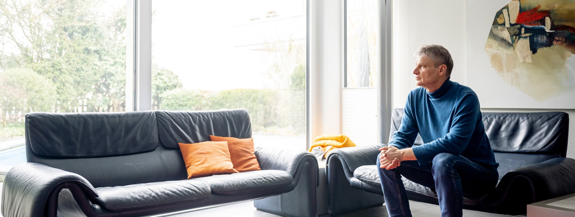 Der Psychologie Guy Bodenmann sitzt auf einen Sofa udn schaut dabei aus dem Fenster