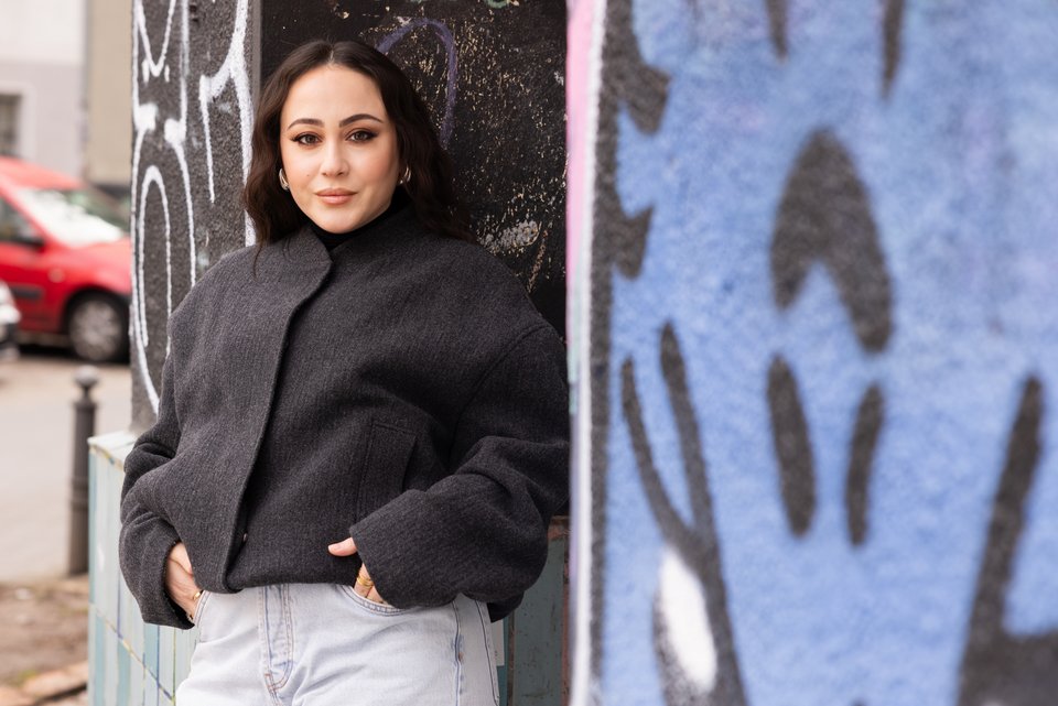 Die Influencerin Hatice Schmidt steht entspannt an eine Graffiti-Wand gelehnt, die Hände in den Hosentaschen und hat keine Angst mehr vor ihrer Herkunft, die von Armut und Gewalt geprägt war