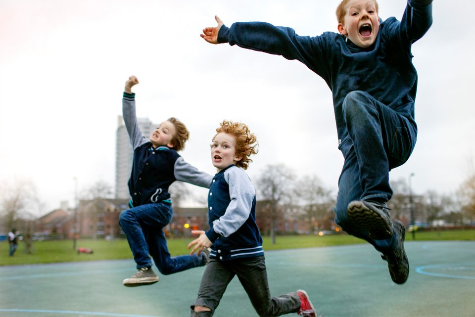 Das Foto zeigt drei Jungs im Grundschulalter, die über einen Platz rennen und springen.