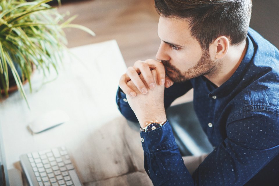 Foto zeigt einen jungen Mann, der nachdenklich am Computer sitzt