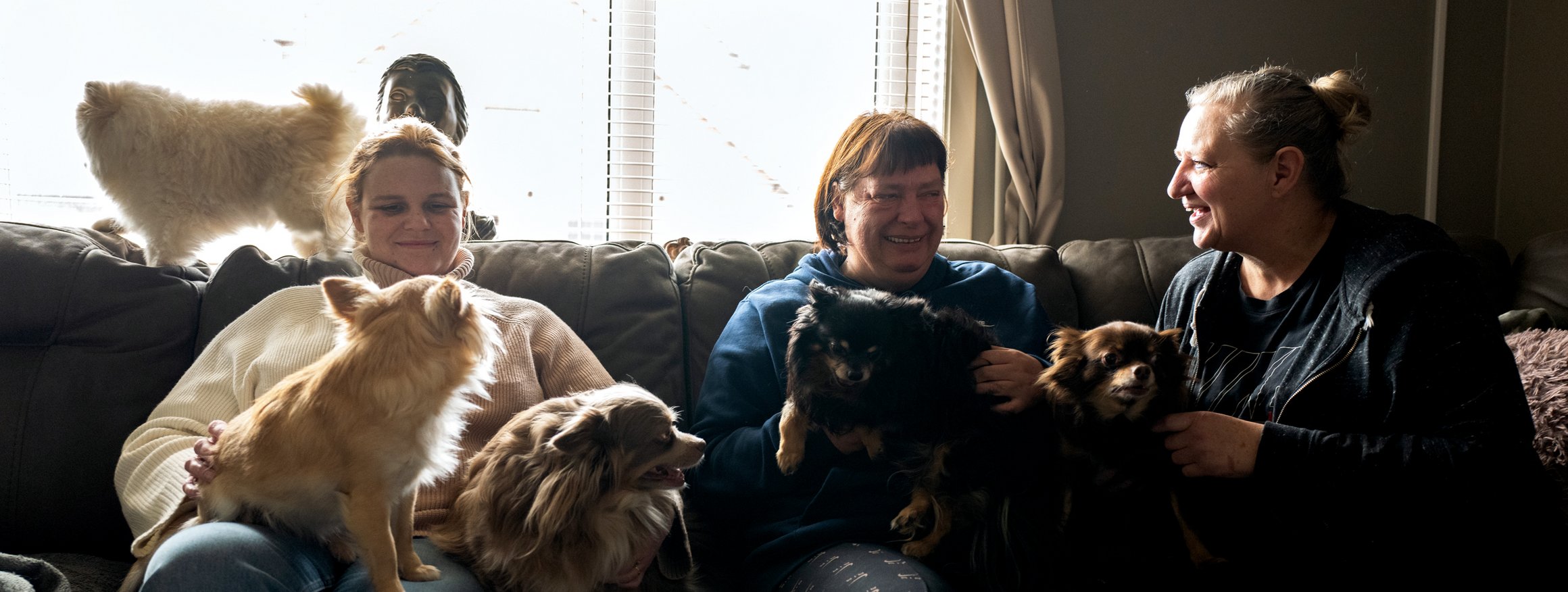 Frauen mit psychischen Erkrankungen sitzen gemeinsam mit ihren Haustieren auf einem Sofa in ihrer WG und lächeln zufrieden