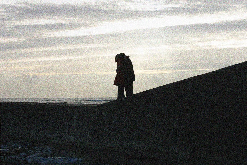 Das Foto zeigt ein Paar, das sich auf eine Steige vor dem Meer umarmt.
