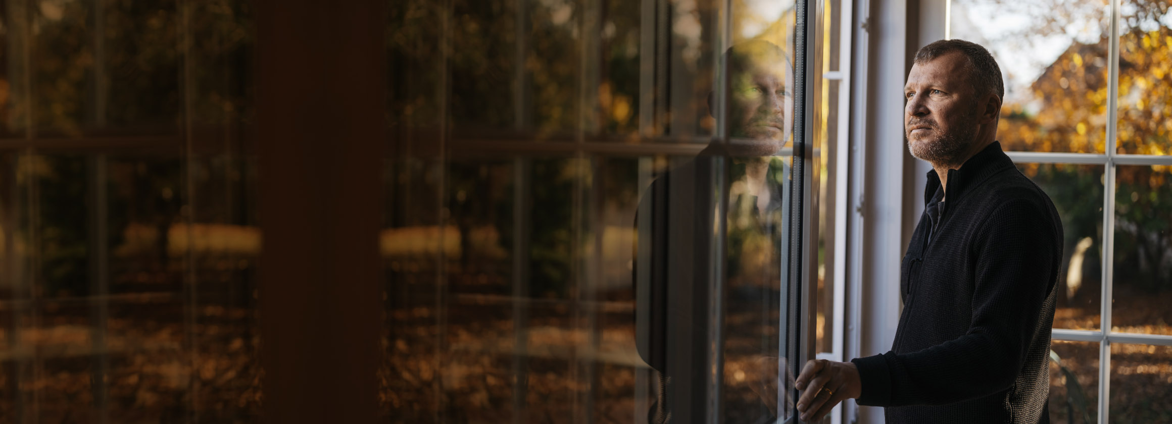 Das Foto zeigt Autor Andreas Maier vor einem spiegelnden Fenster mit Wald.